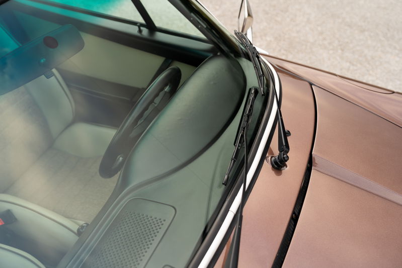 Close-up of a 1975 copper brown metallic Porsche 911 Carrera interior, showing windshield wipers and cream upholstery.
