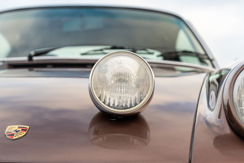 Front view of a metallic copper brown 1975 Porsche 911 Carrera with chrome headlight trim and emblem.
