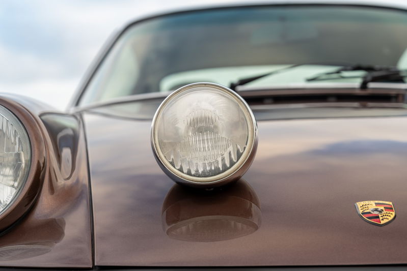 Close-up of a 1975 Porsche 911 Carrera in Copper Brown Metallic, featuring a fog light.