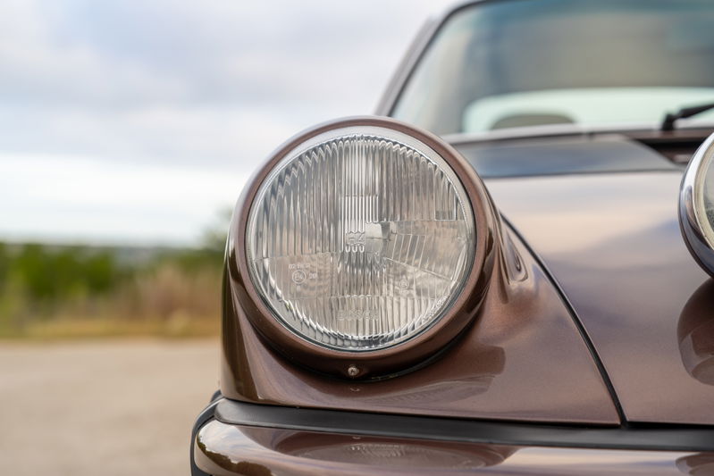 Close-up of the iconic round headlight on a copper brown metallic 1975 Porsche 911 Carrera.