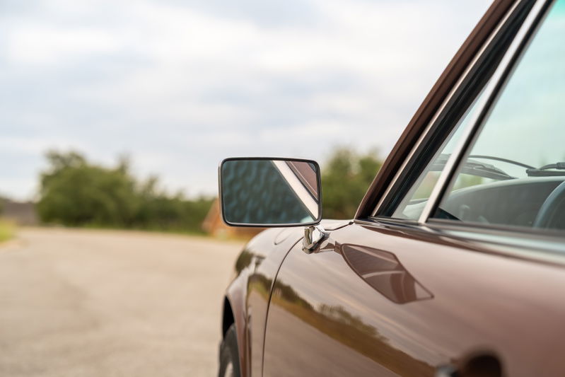 Close-up of a copper brown metallic 1975 Porsche 911 Carrera door and side mirror.