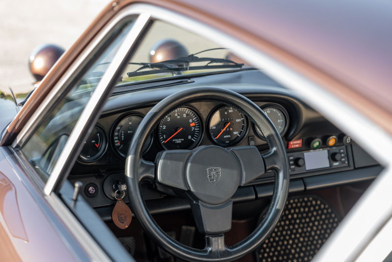 Porsche 911 Carrera interior with classic gauges, black steering wheel, and copper-brown metallic exterior trim.