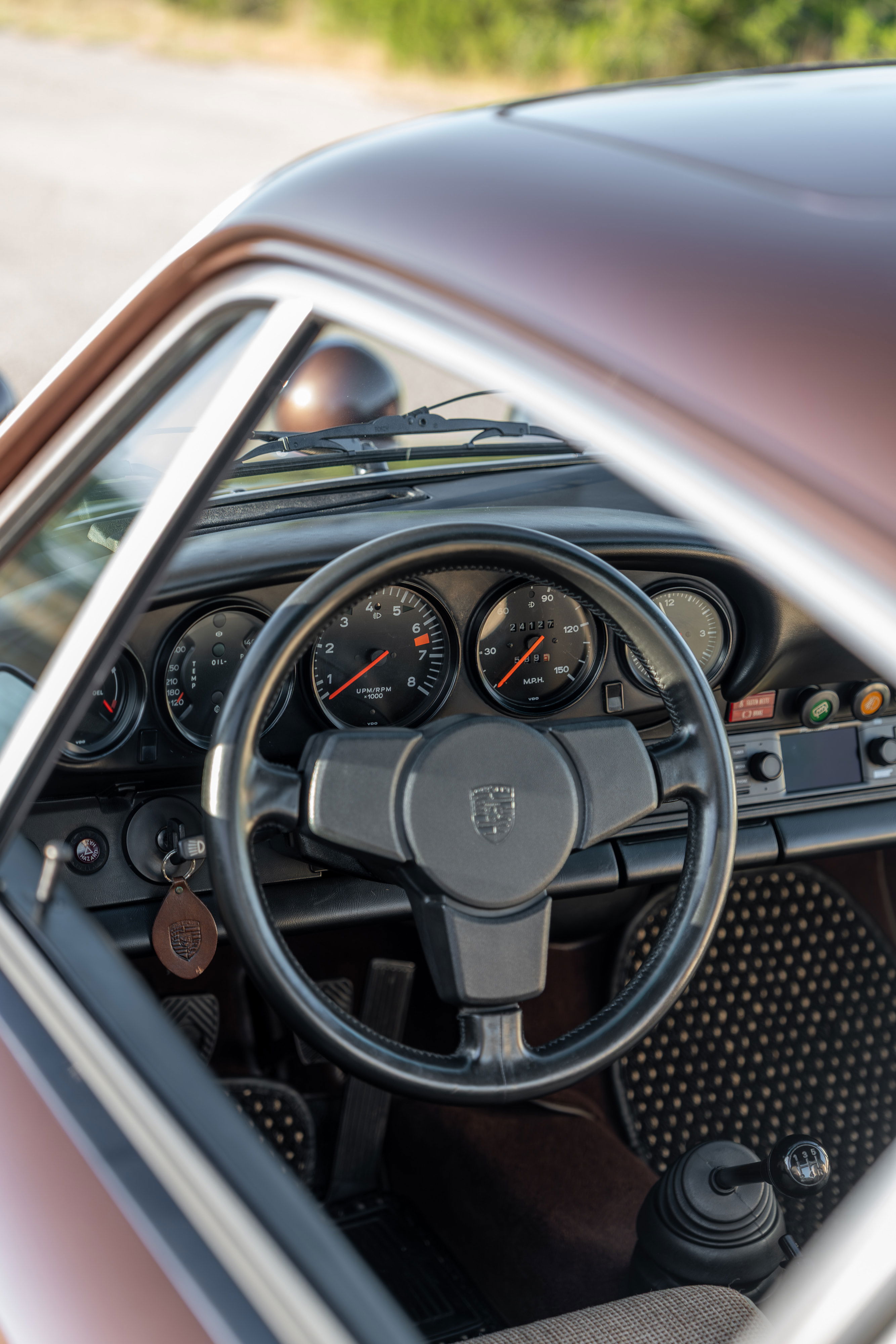 Interior view of a 1975 Porsche 911 Carrera in Copper Brown Metallic, showing dashboard and steering wheel.