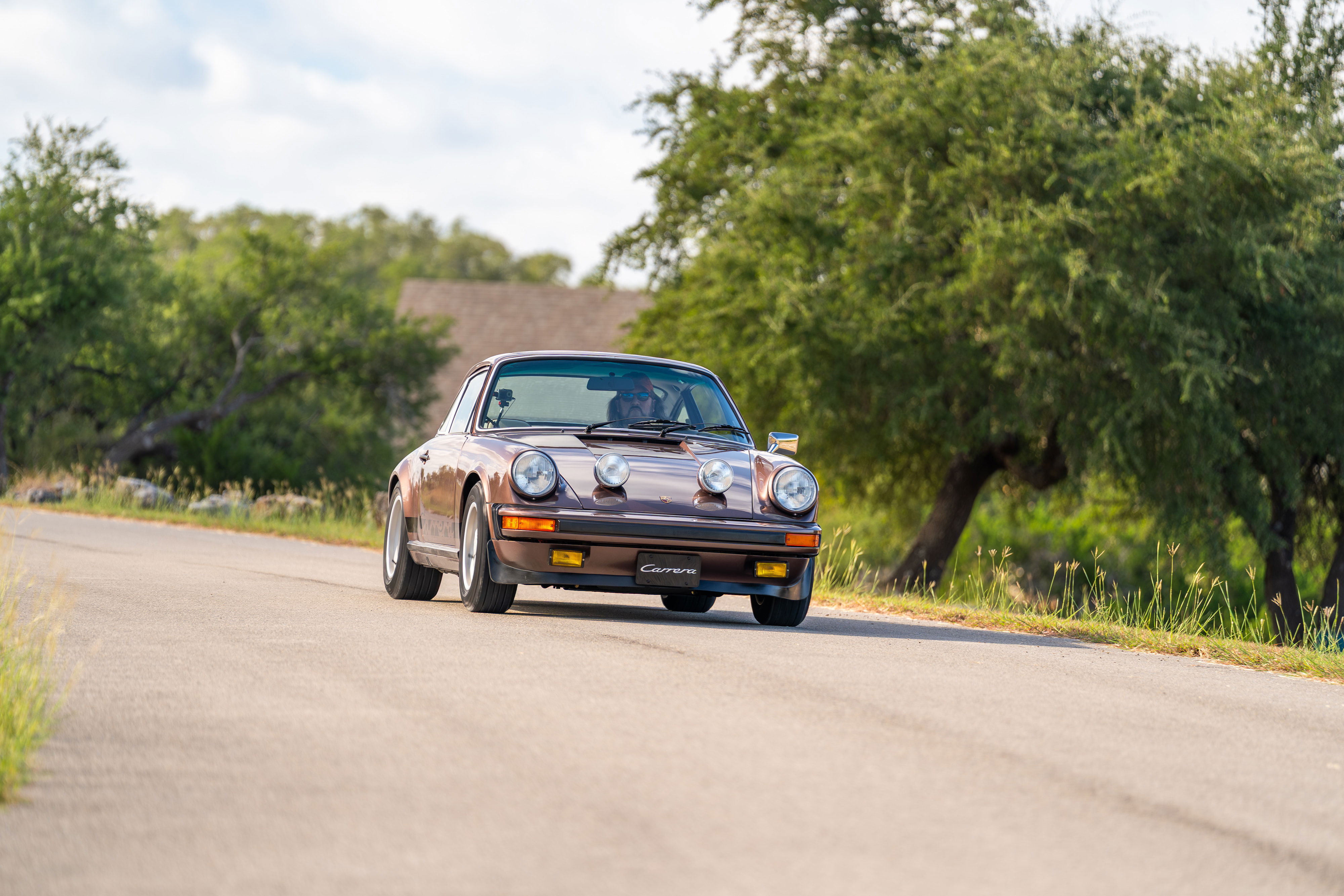 1975 Porsche 911 Carrera in Copper Brown Metallic driving on a country road.