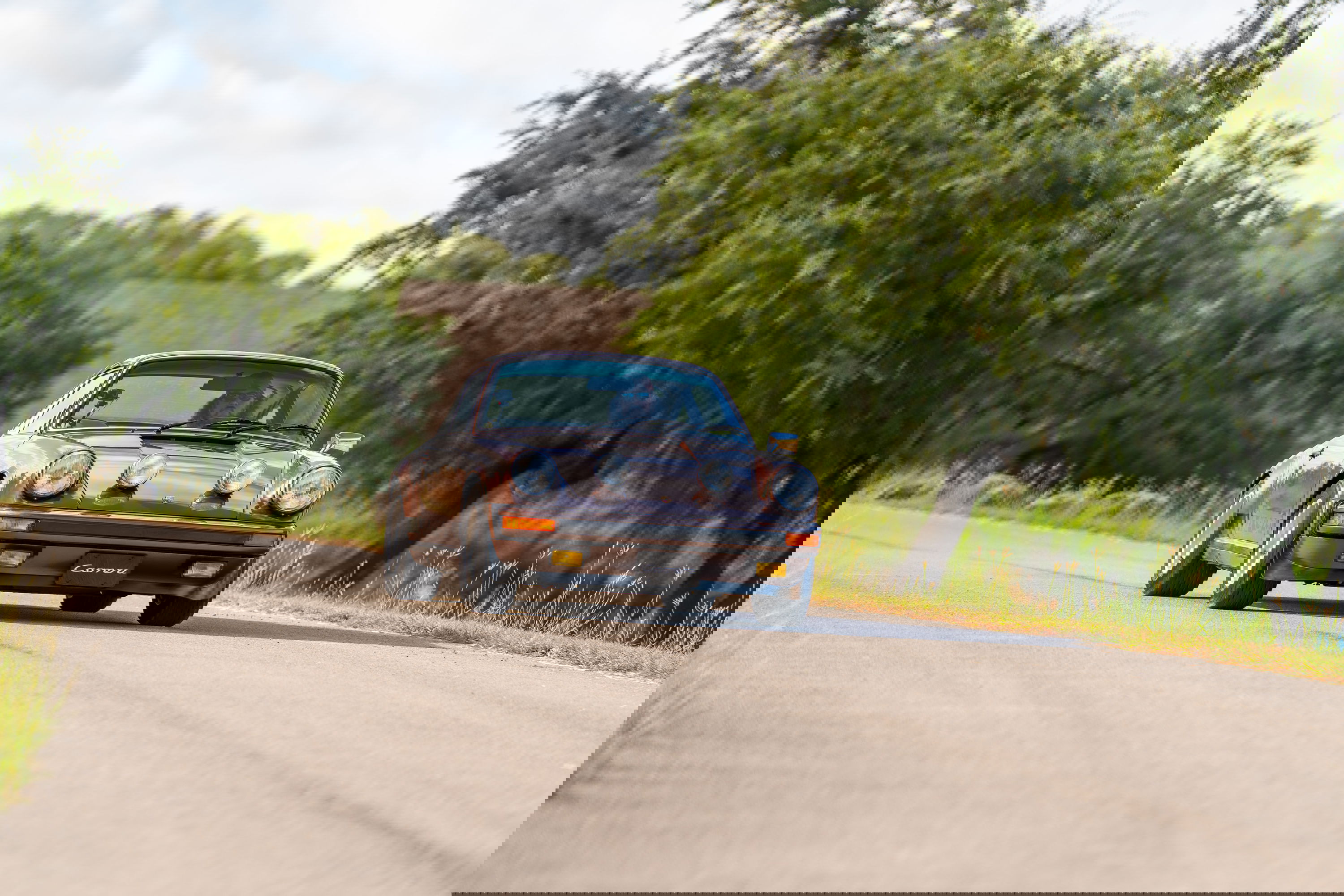 1975 Porsche 911 Carrera in Copper Brown Metallic driving on a country road.