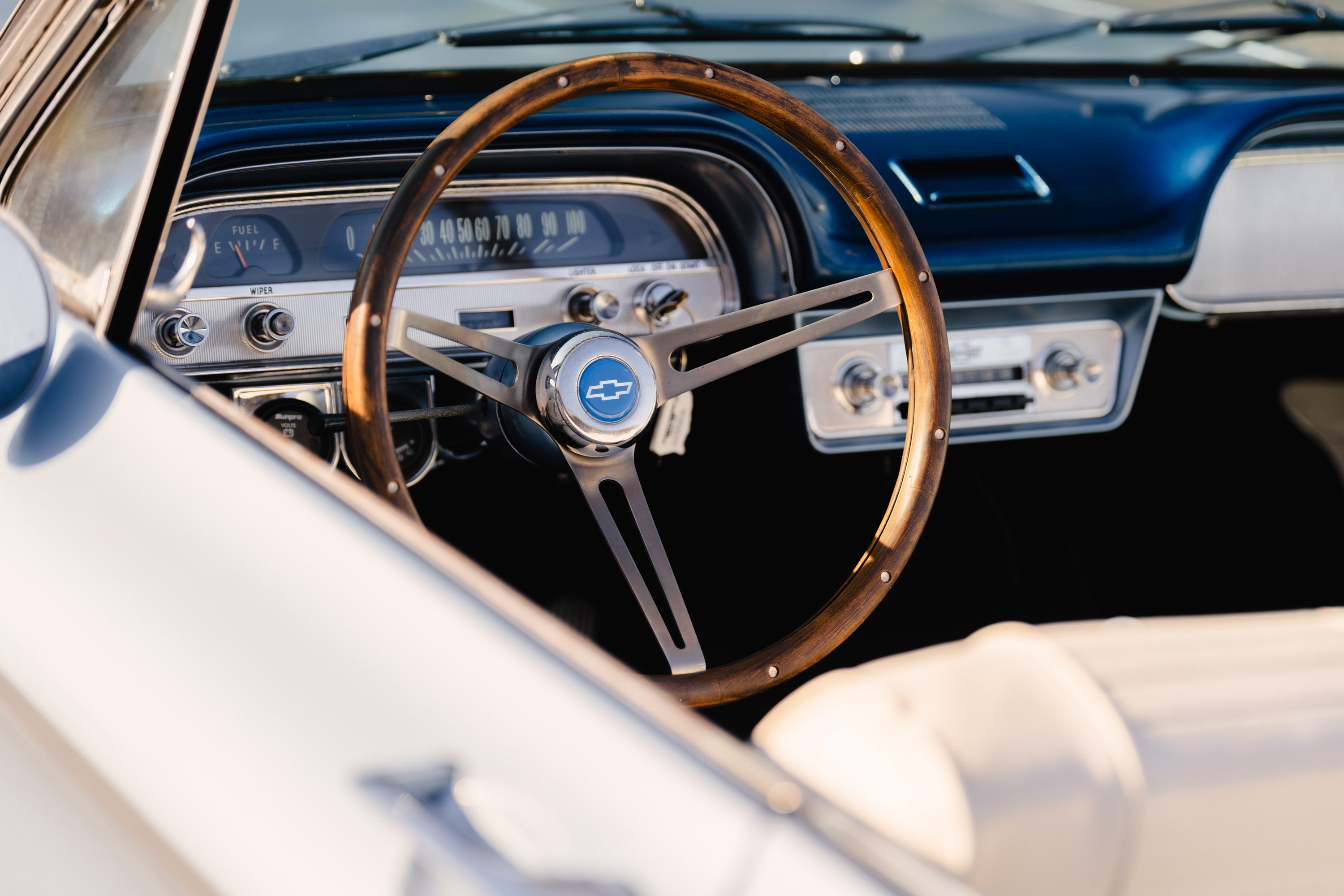 Close-up of a 1966 Chevrolet Corvair convertible interior. Features wooden steering wheel with bowtie emblem and retro radio.