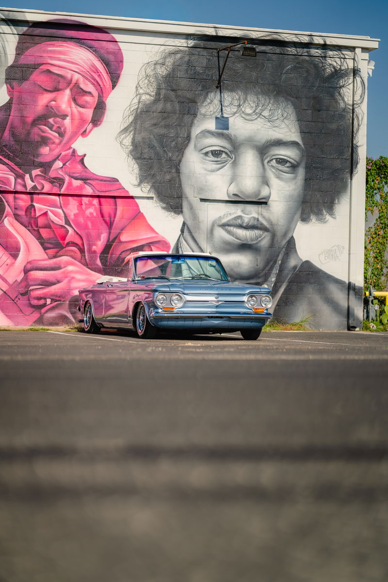 Blue metallic 1966 Chevrolet Corvair convertible with chrome rims and white soft top.