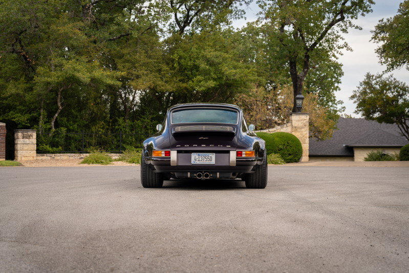 Rear view of an aubergine metallic 1990 Singer Porsche 911 with chrome trim and dual exhaust.