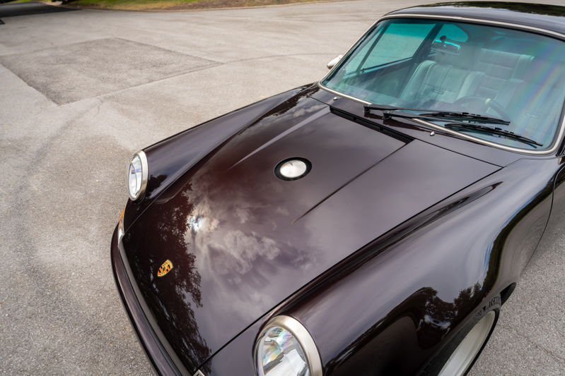 Front view of a 1990 Singer Porsche 911 in Aubergine Metallic. Classic headlights and hood trim.