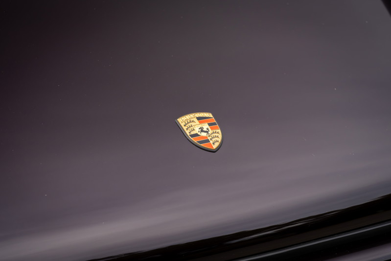 The Porsche crest emblem on the hood of an aubergine metallic 1990 Singer Porsche 911.