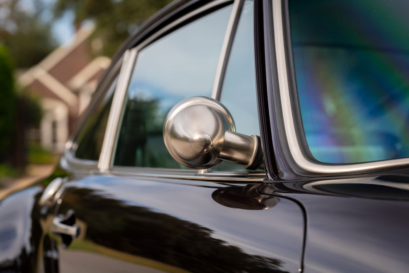 Closeup of a black 1990 Singer Porsche 911, showing the chrome side mirror and window trim.