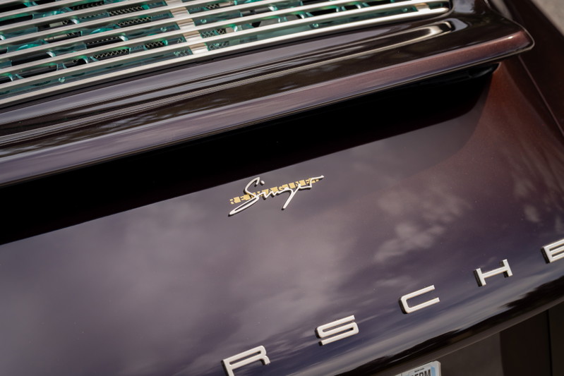 1990 Singer Porsche 911 in aubergine metallic. Close-up on gold Singer badging and chrome Porsche lettering.