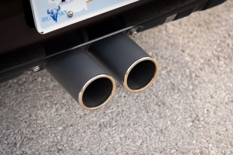 Close-up of dual matte black exhaust tips with polished chrome rims on an aubergine metallic 1990 Singer Porsche 911.