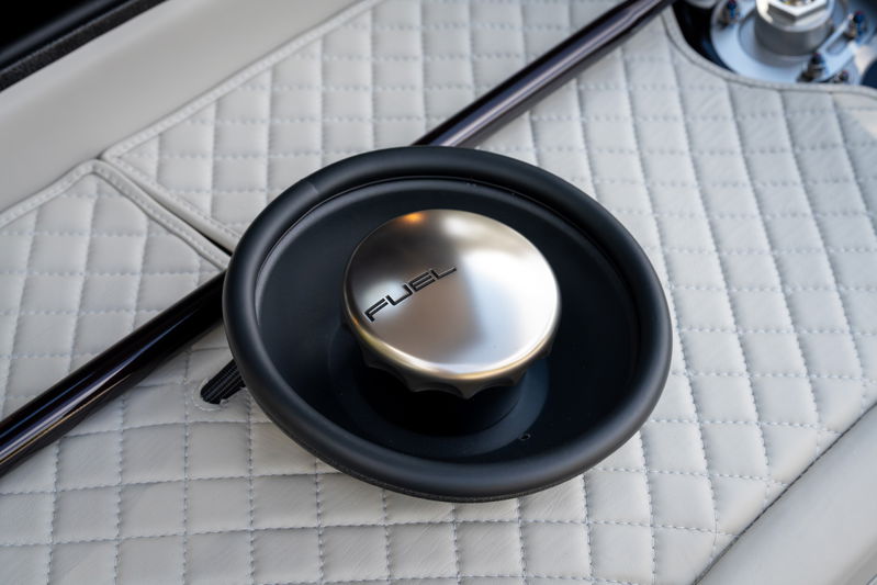 Close-up of brushed aluminum fuel cap with "FUEL" text on quilted white interior trim of a 1990 Singer Porsche 911.