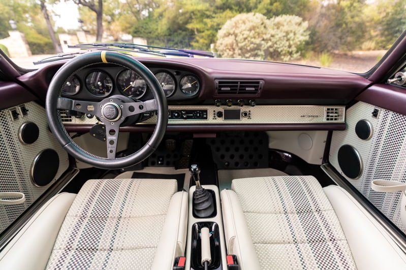 Interior view of an aubergine metallic 1990 Singer Porsche 911, featuring a classic steering wheel & plaid seats.