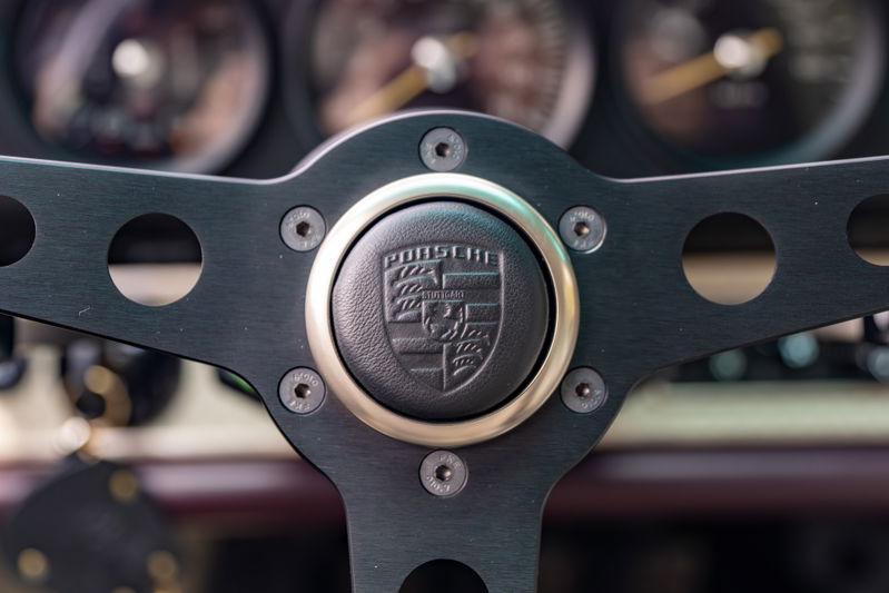 Close-up of a 1990 Singer Porsche 911 steering wheel with Porsche crest.