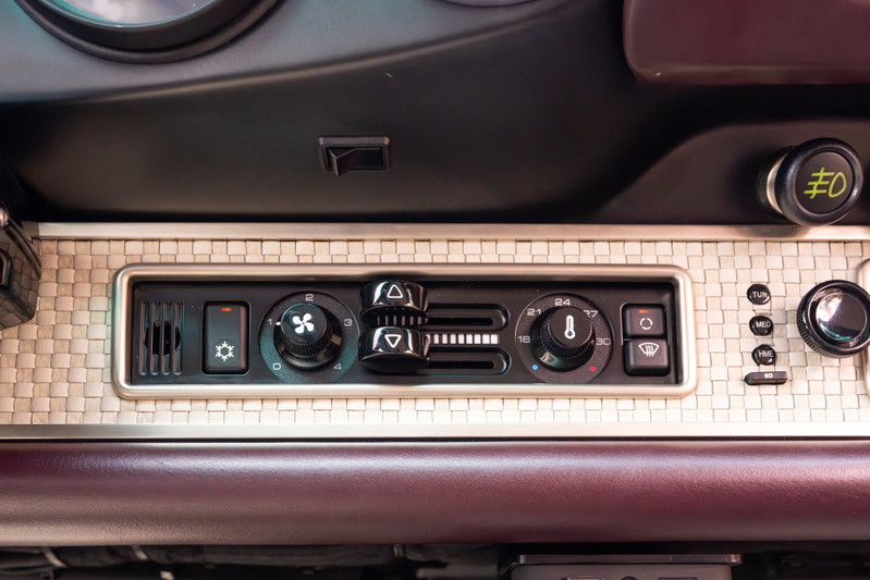 Interior shot of a 1990 Singer Porsche 911's climate control panel with metallic weave trim.