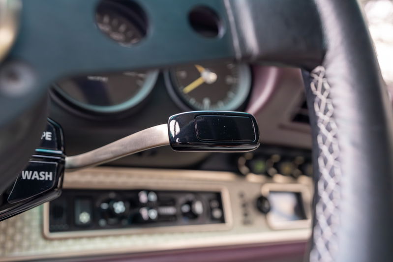 Close-up of the steering column stalk, tachometer, and dashboard controls of an aubergine metallic 1990 Singer Porsche 911.