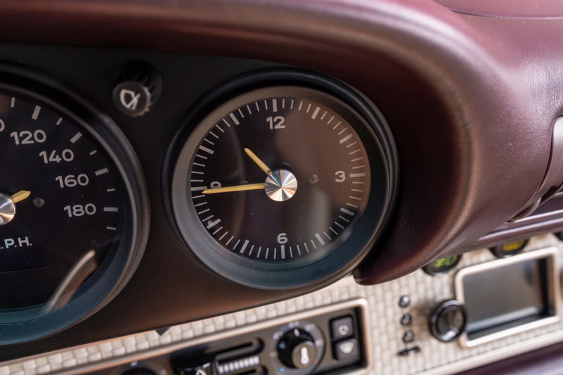 Classic dashboard in a 1990 aubergine metallic Singer 911, featuring a tachometer and clock.