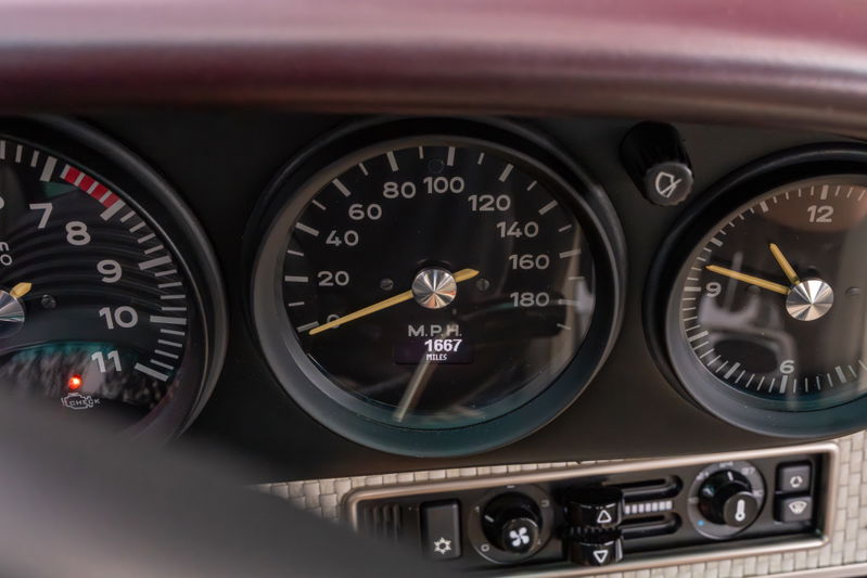 Close-up of aubergine metallic 1990 Singer Porsche 911 dashboard with analog gauges.