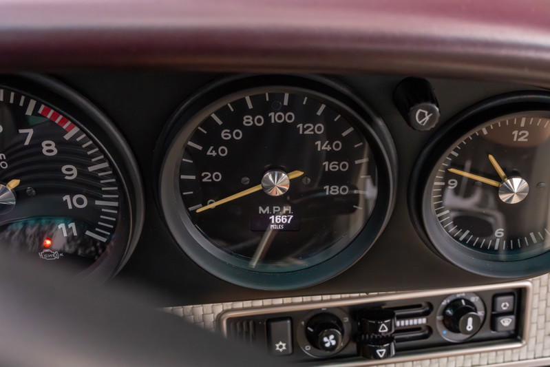 Close-up of aubergine metallic 1990 Singer Porsche 911 dashboard with analog gauges.