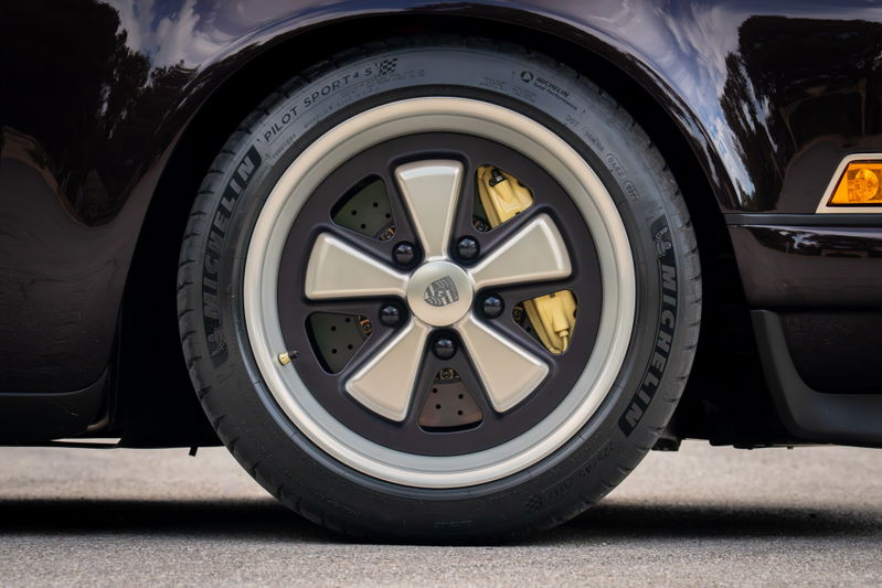 Close-up of an Aubergine Metallic 1990 Singer Porsche 911 wheel, with gold brake calipers and Michelin Pilot Sport tires.