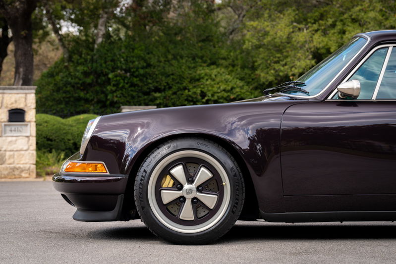 Close up of an aubergine metallic 1990 Singer Porsche 911 with Fuchs wheels and yellow brake calipers.