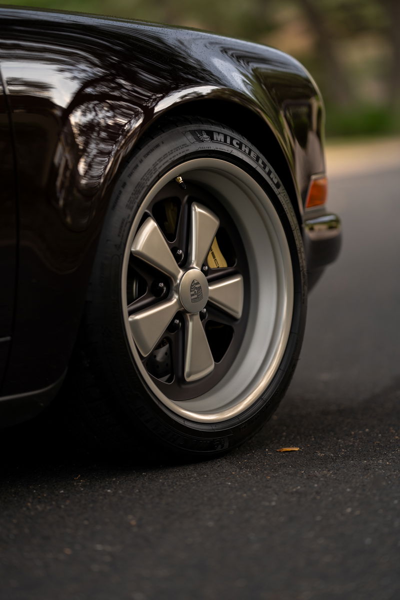 Close-up of an aubergine metallic 1990 Singer Porsche 911 with Fuchs rims and yellow brake calipers.
