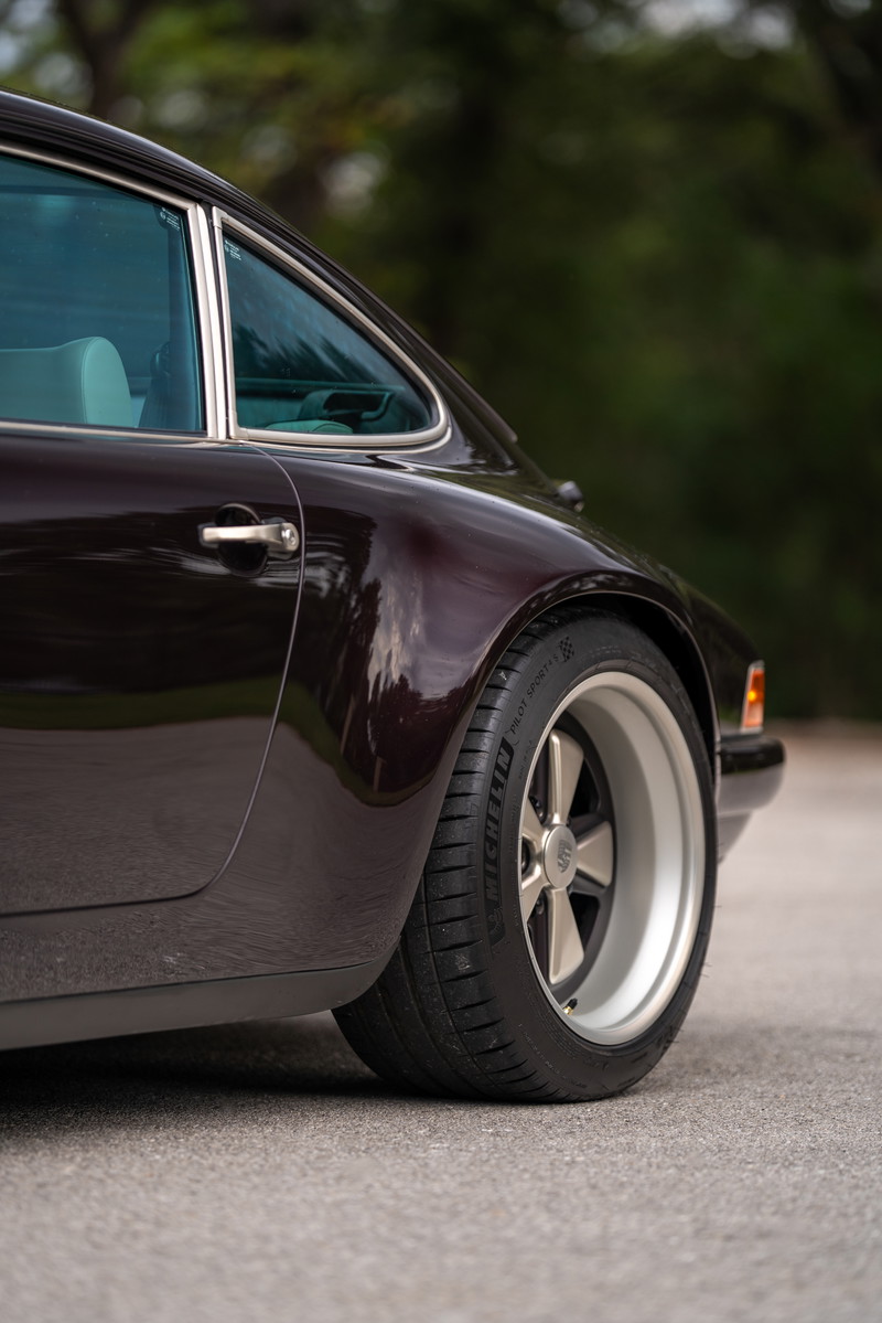 Aubergine Metallic 1990 Singer Porsche 911 rear quarter view showing alloy rims and chrome trim.