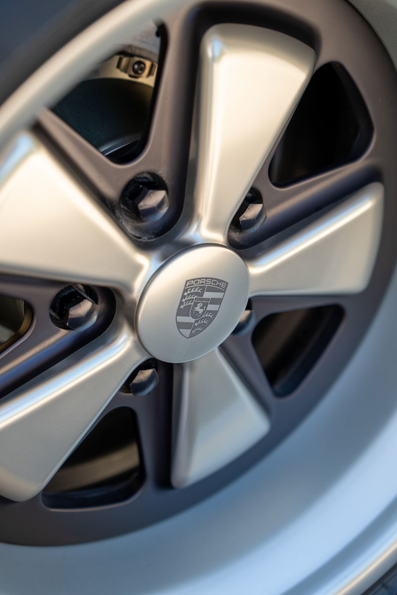 Close-up of a 1990 Porsche 911's brushed metal five-spoke alloy rim with the Porsche crest center cap.