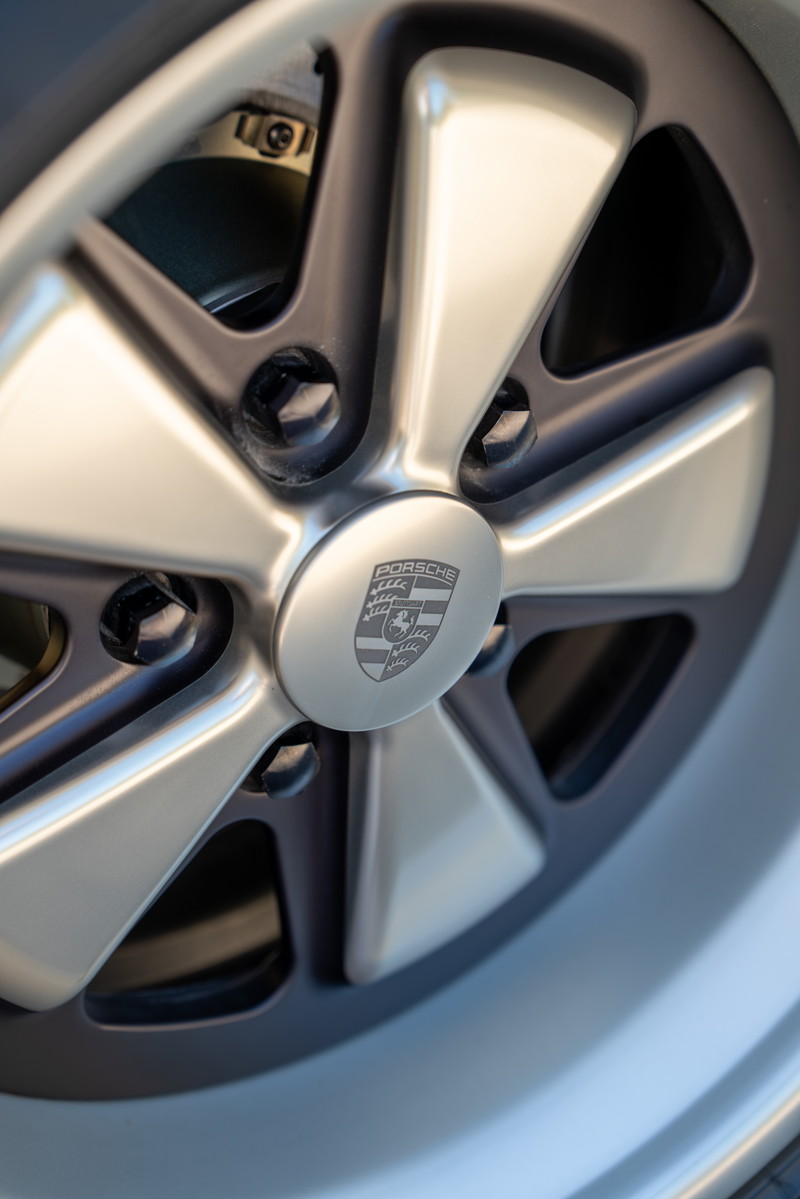 Close-up of a 1990 Porsche 911's brushed metal five-spoke alloy rim with the Porsche crest center cap.