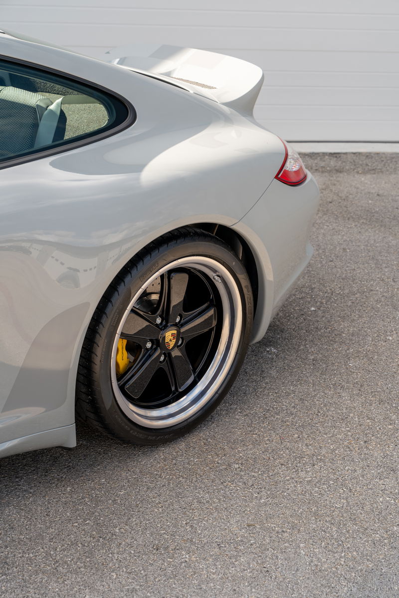 Rear three-quarter view of a grey 2010 Porsche 911 Sport Classic with black five-spoke rims.