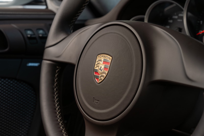 Close up on the dark interior of a 2010 Porsche 911 Sport Classic, showing the steering wheel with the Porsche crest.