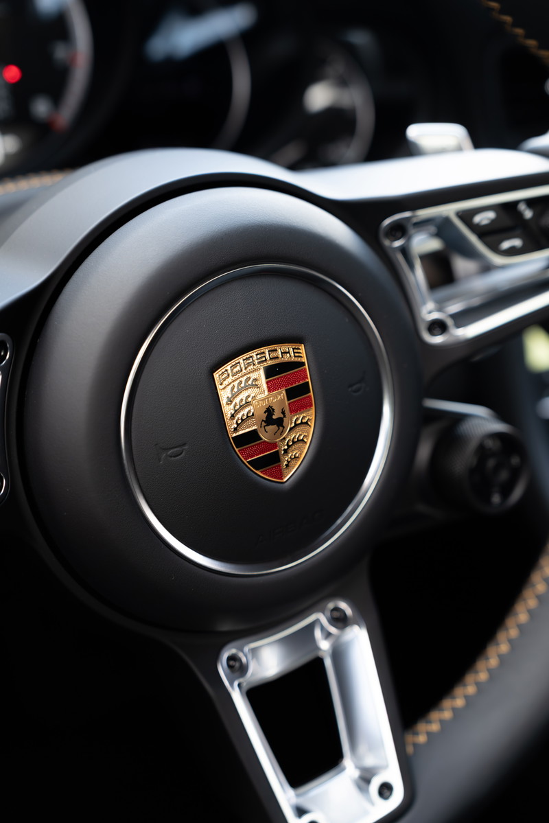Close-up of a black 2018 Porsche 911 Turbo S Exclusive Series steering wheel with silver trim and Porsche crest.