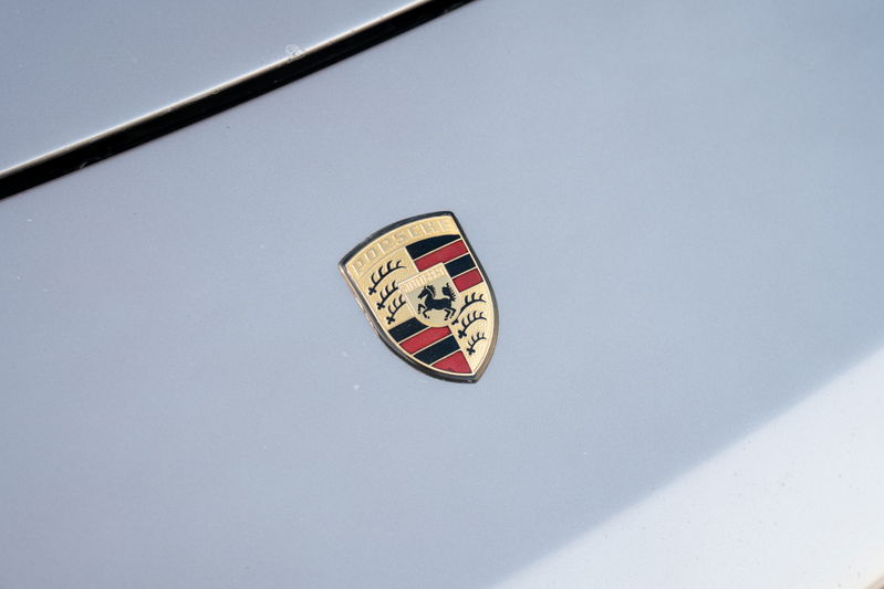 Close-up of a vintage Porsche crest emblem on the hood of a silver 1987 Porsche 944 Turbo S.