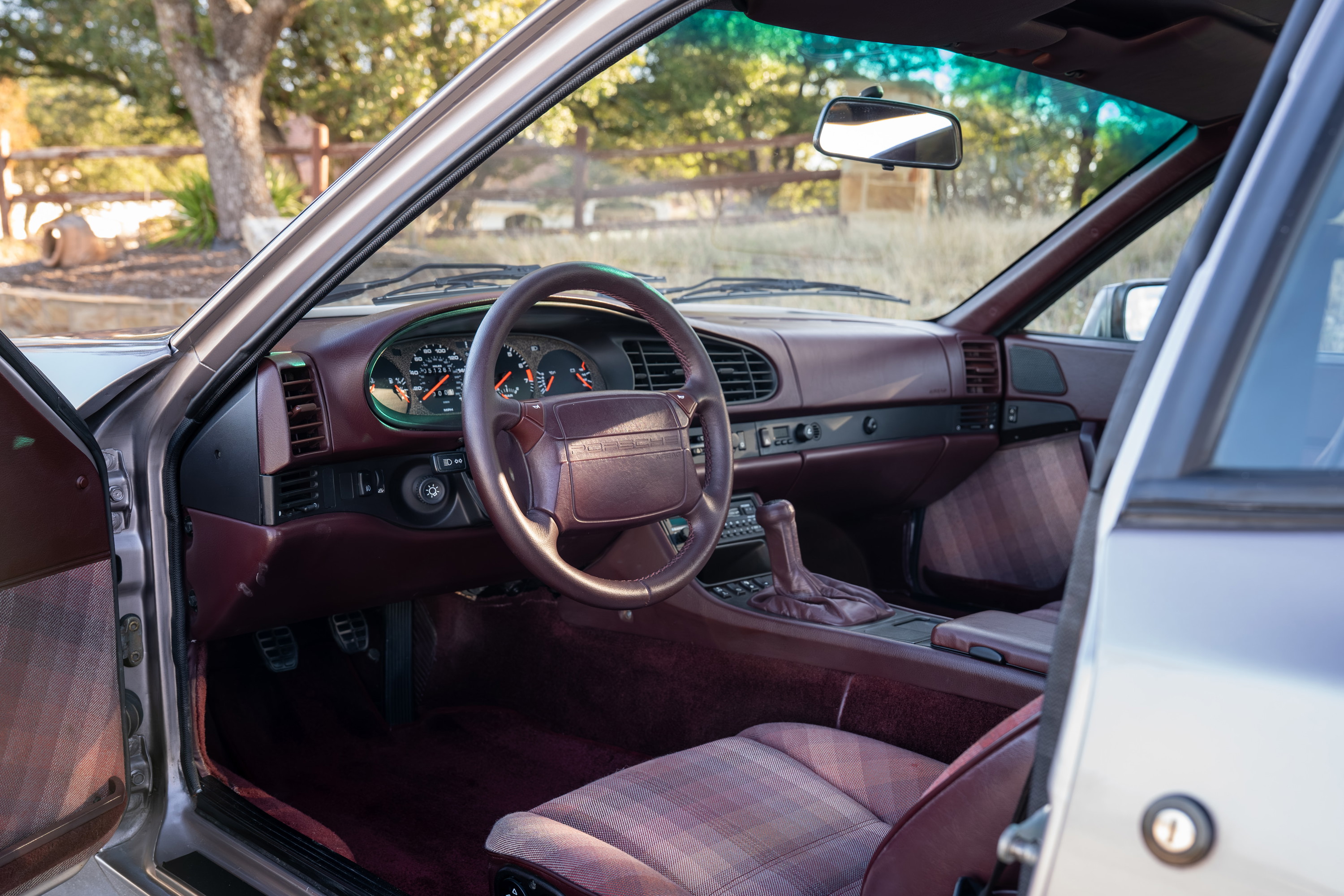 Silver 1987 Porsche 944 Turbo S interior with burgundy dash, plaid seats, and manual shifter.