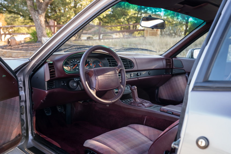 Silver 1987 Porsche 944 Turbo S interior with burgundy dash, plaid seats, and manual shifter.