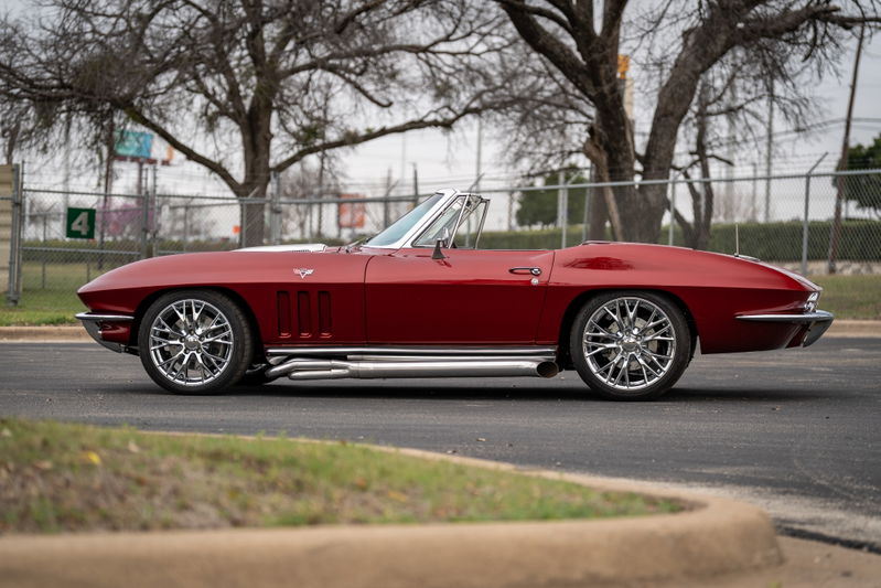 1965 Chevrolet Corvette convertible in red with chrome side pipes and custom chrome rims.