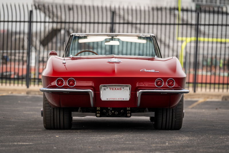 Rear view of a red 1965 Chevrolet Corvette convertible with quad taillights and chrome bumper.