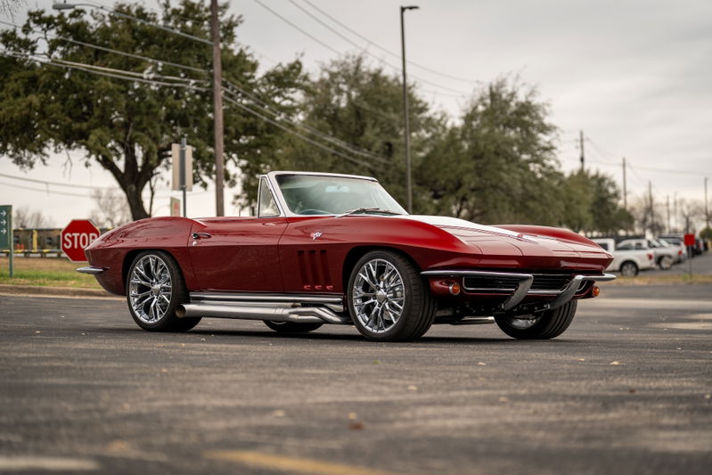 A red 1965 Chevrolet Corvette convertible with chrome side pipes and custom rims.