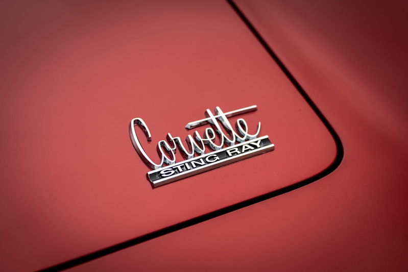 Close-up of a chrome "Corvette Sting Ray" emblem on the red body panel of a 1965 Chevrolet Corvette.