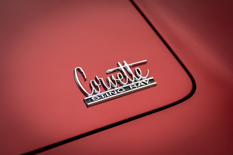 Close-up of a chrome "Corvette Sting Ray" emblem on the red body panel of a 1965 Chevrolet Corvette.