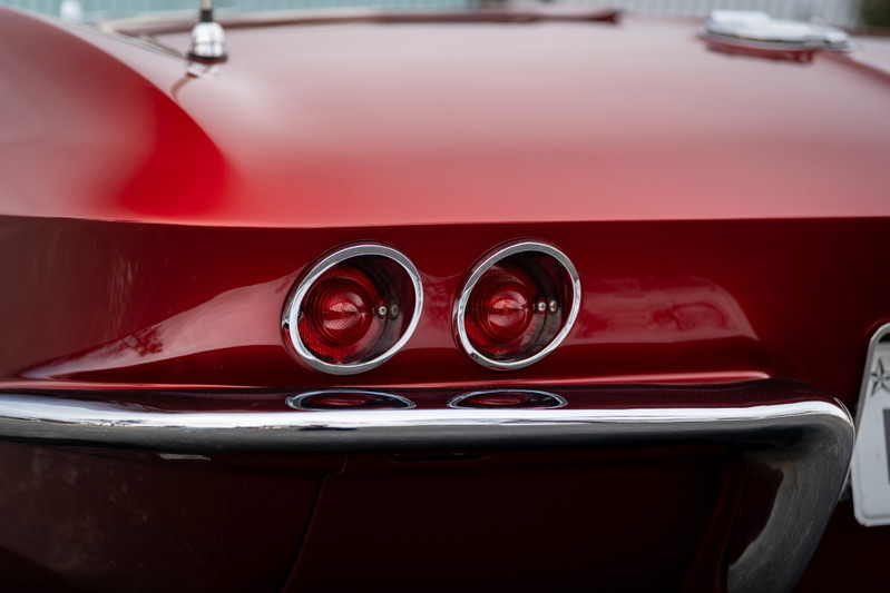 Close up of the iconic dual round taillights and chrome bumper on a red 1965 Chevrolet Corvette.