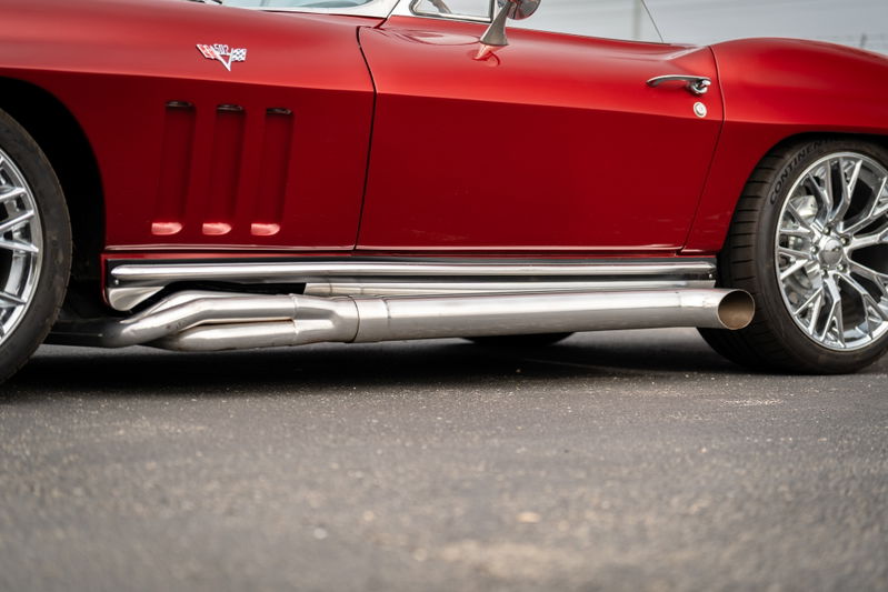 Red 1965 Chevrolet Corvette with side exhaust pipes and chrome rims.