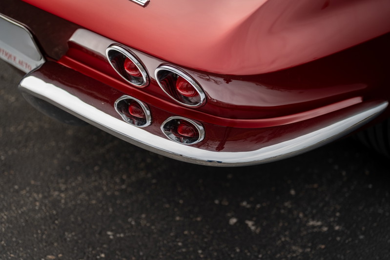 Close-up of a red 1965 Chevrolet Corvette's quad tail lights and chrome bumper trim.