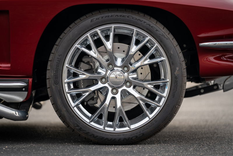 Close-up of a chrome multi-spoke wheel and drilled rotors on a red 1965 Chevrolet Corvette.