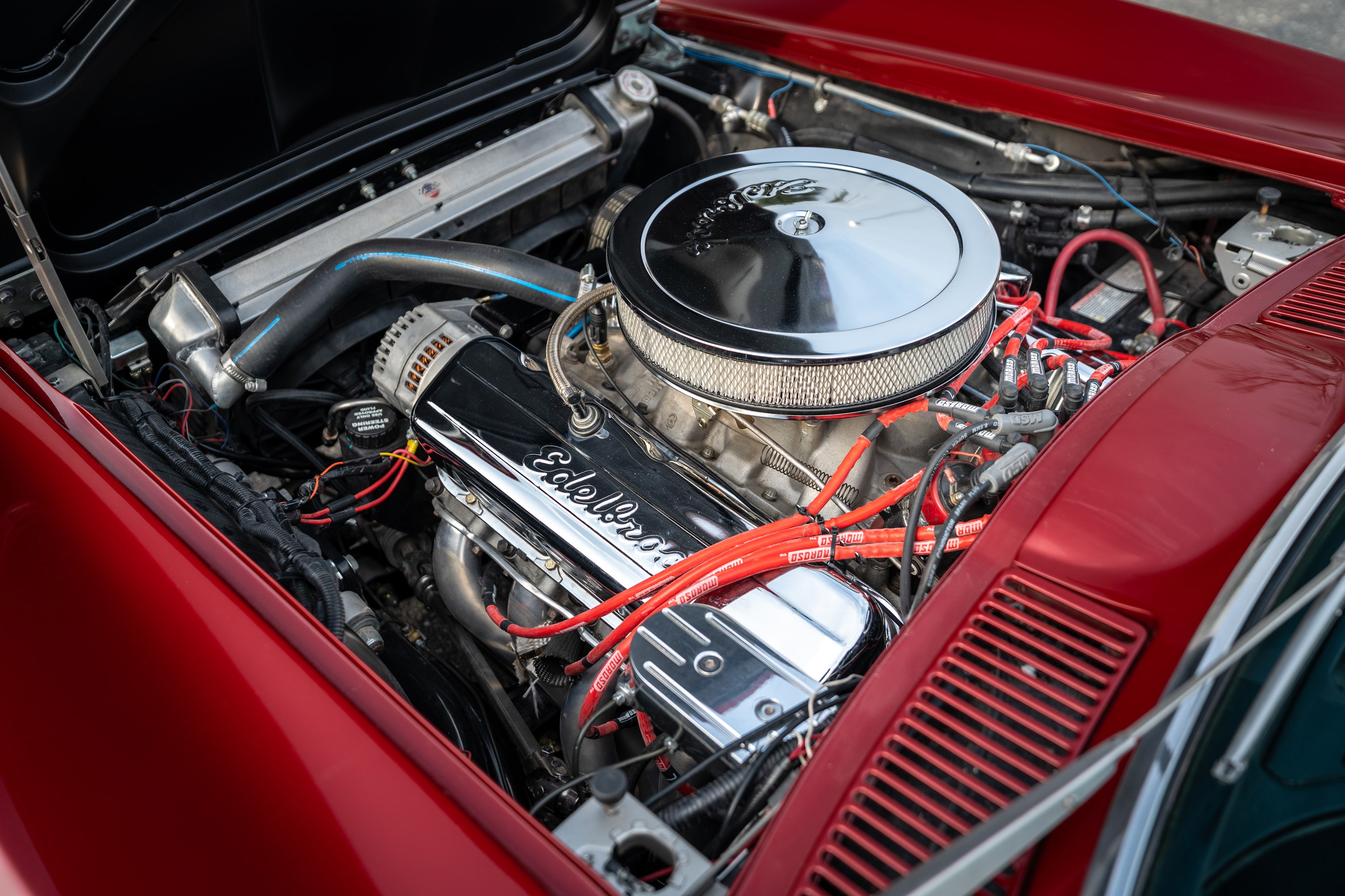 Red 1965 Chevrolet Corvette engine bay with Edelbrock valve covers and chrome air cleaner.
