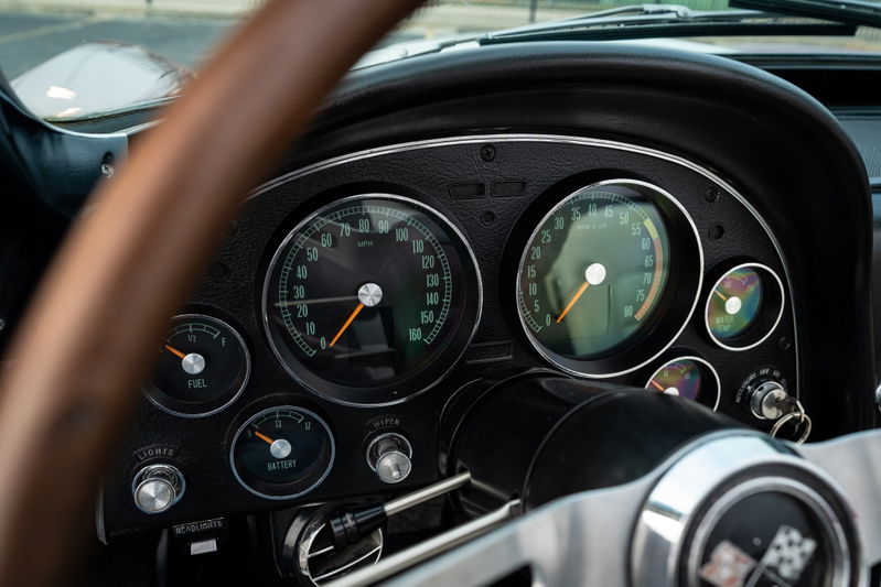 1965 Chevrolet Corvette dashboard with analog gauges and a wooden steering wheel.