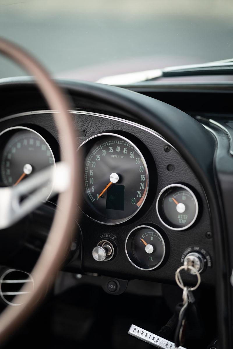 Close-up of a 1965 Chevrolet Corvette's dashboard, featuring classic gauges and a wooden steering wheel.