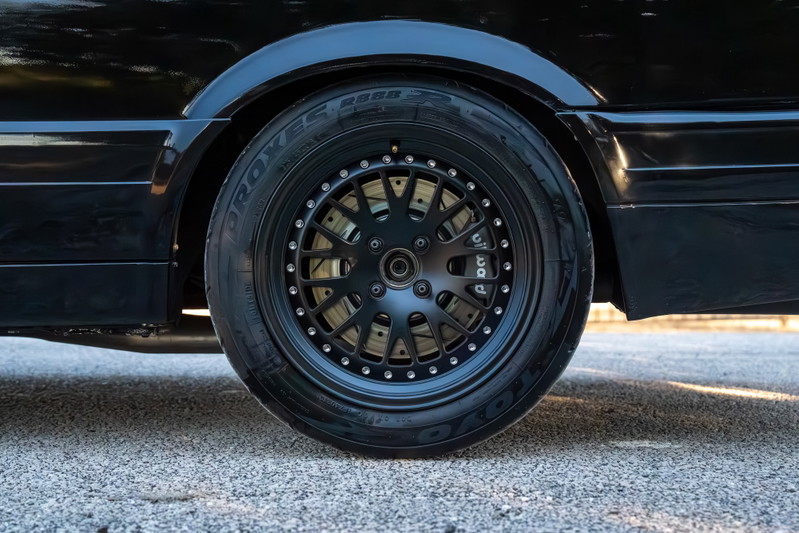 Black 1989 BMW 325is with black multi-spoke rims and performance brake calipers.